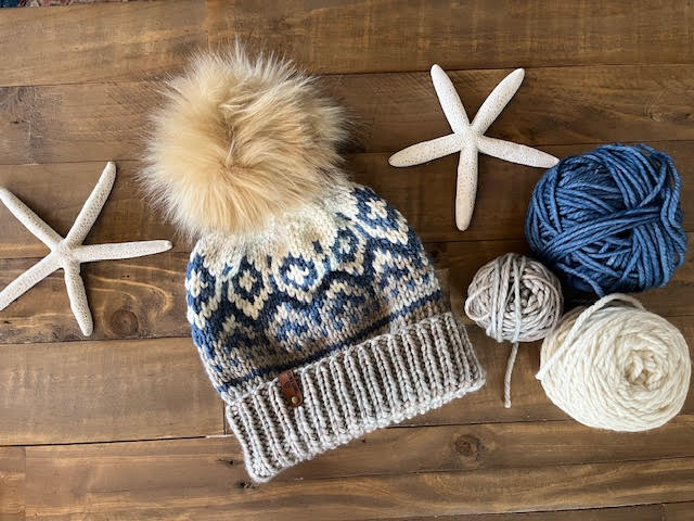 Knitted hat with pom-pom and yarn balls on a wooden surface