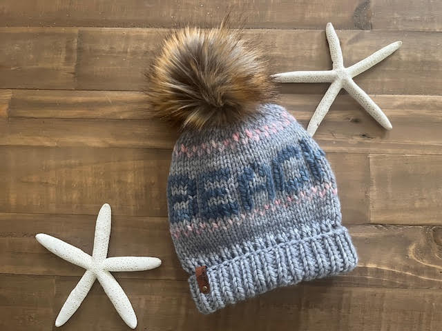 Knitted hat with a pom-pom on a wooden surface with starfish