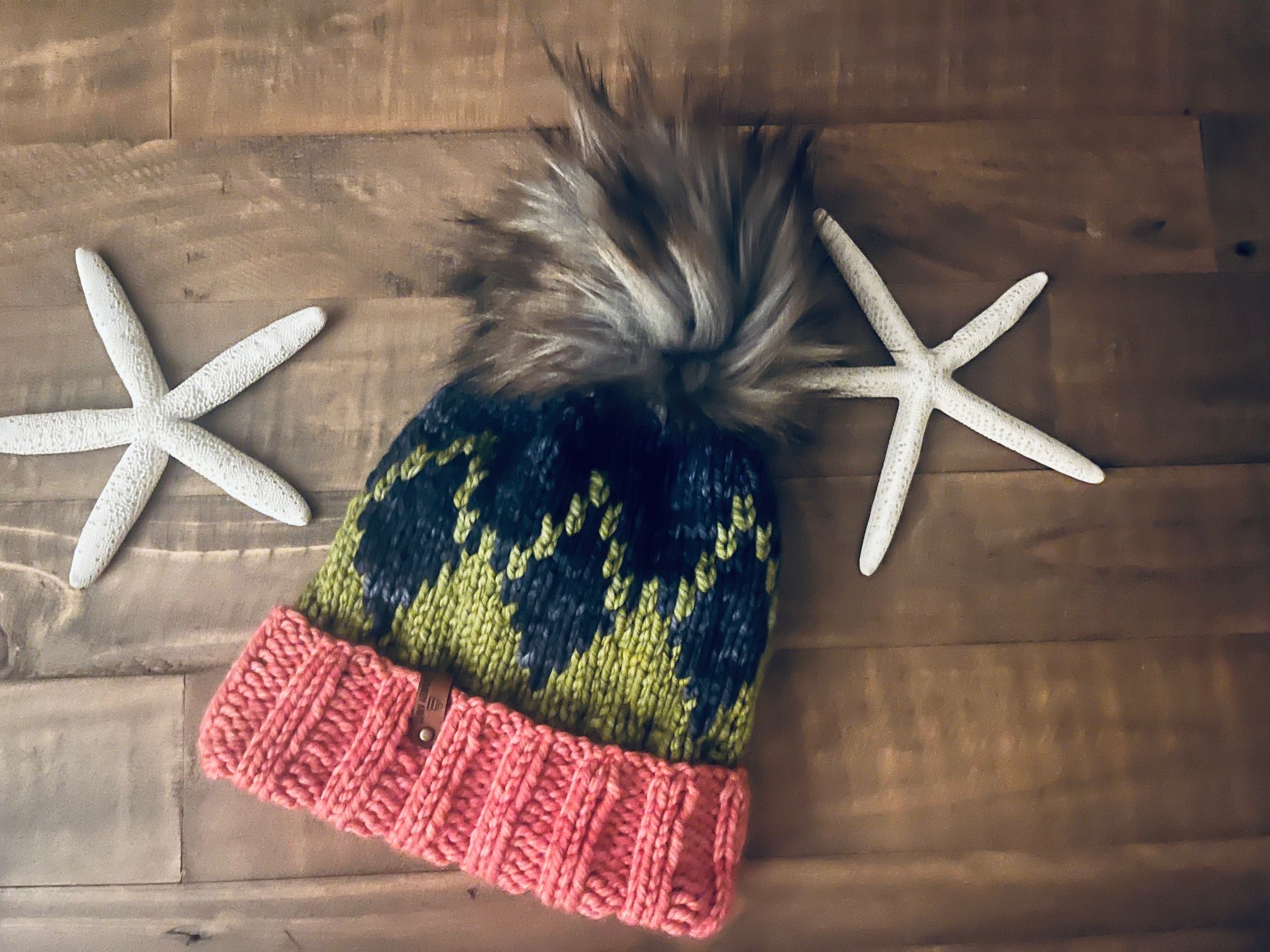 Knitted hat with a pom-pom on a wooden surface with starfish