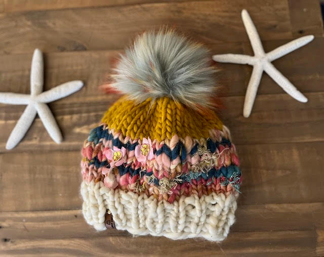 Knitted multicolored beanie with a pom-pom on a wooden surface with starfish.